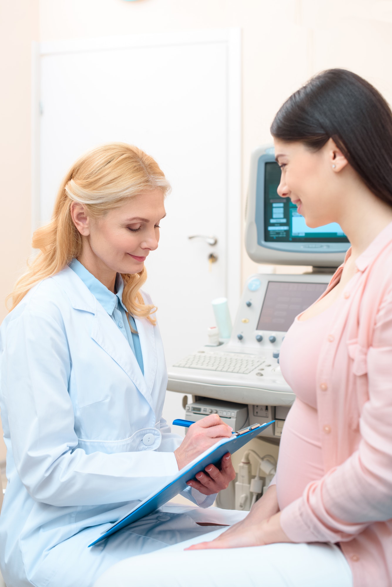 obstetrician gynecologist consulting happy young pregnant woman and writing in clipboard